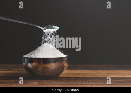 Le sucre versé dans un bol en acier sur une table en bois. Concept de la mauvaise alimentation et le diabète Banque D'Images