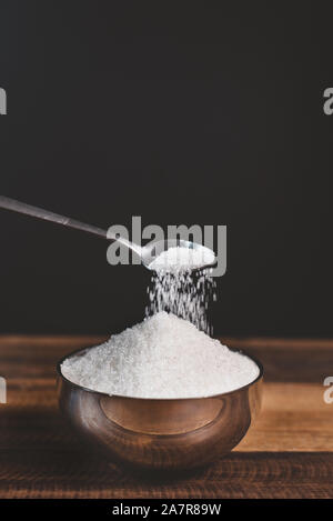 Le sucre versé dans un bol en acier sur une table en bois. Concept de la mauvaise alimentation et le diabète Banque D'Images
