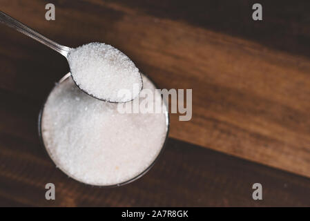 Le sucre versé dans un bol en acier sur une table en bois. Concept de la mauvaise alimentation et le diabète Banque D'Images