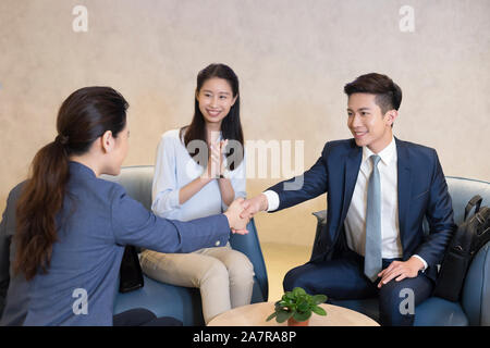 Photo de deux jeunes hommes et femmes d'affaires se serrer la main lors d'une réunion avec un autre l'un des mains et souriant Banque D'Images