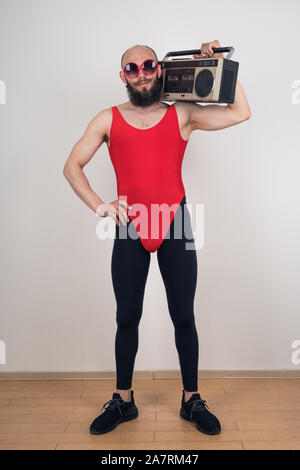 Un homme habillé pour soirée disco-rétro parties. Funny guy barbus dans des lunettes de soleil et avec body avec magnétophone rétro Banque D'Images