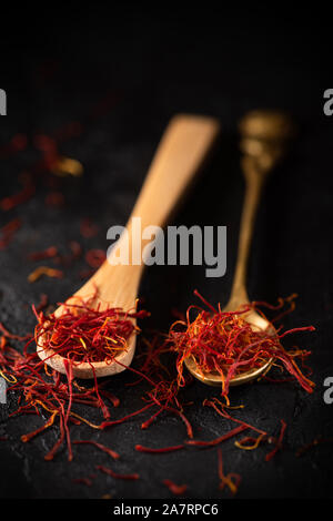 Épices safran filets dans les cuillères sur la table en pierre d'ardoise noire. La saveur du safran et la coloration des ingrédients d'assaisonnement. Banque D'Images