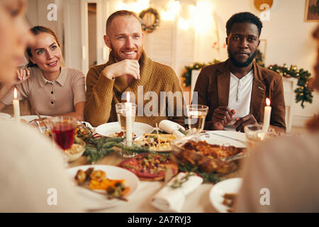Poirtrait de groupe multi-ethnique de personnes appréciant le dîner assis à table avec de la nourriture délicieuse, l'accent sur l'homme barbu souriant dans le centre Banque D'Images