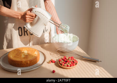 Fouetter la crème mains d'hommes blancs dans un bol en verre avec le mélangeur sur table en bois. Décisions ou gâteau Red Velvet Cake Banque D'Images