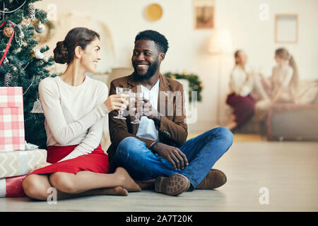 Portrait de couple moderne assis par arbre de Noël et de cliquetis verres de champagne à la maison, copy space Banque D'Images