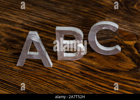 Le mot ABC avec des lettres en métal blanc, debout sur un fond de bois brun foncé avec focus sélectif. Banque D'Images