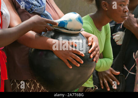 Les mains d'une femme portant un pot de bière zoulou noir contenant de la bière au marula Marula Tembe festival dans le KwaZulu-Natal, Afrique du Sud. Banque D'Images