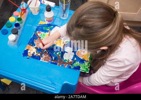 Jeune fille assise à une petite table dans la cuisine la peinture d'une image colorée pour le plaisir Banque D'Images