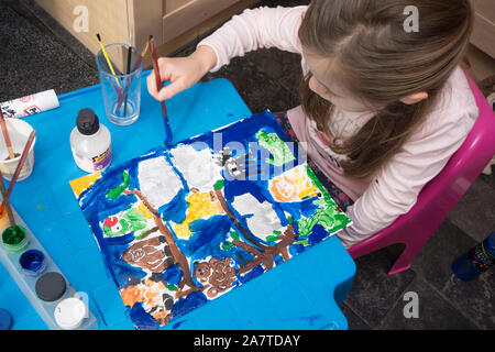 Jeune fille assise à une petite table dans la cuisine la peinture d'une image colorée pour le plaisir Banque D'Images