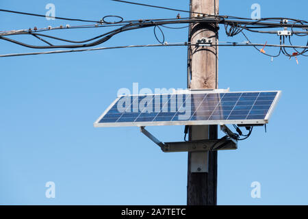 Close up d'un panneau solaire sur un poteau de téléphone avec des fils au-dessus et un ciel bleu derrière Banque D'Images