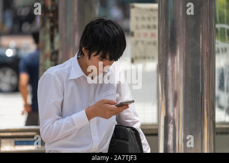 Close up d'un homme japonais assis et reposant sur un arrêt de bus avec un téléphone dans ses mains à Shibuya à Tokyo, Japon. Banque D'Images