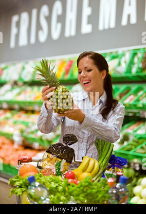 Frau geht Einkaufen im Dach Photovoltaik, kauft eine Ananas, Einkaufswagen mit Obst, Gemüse und Lebensmittel, M. : Oui Banque D'Images