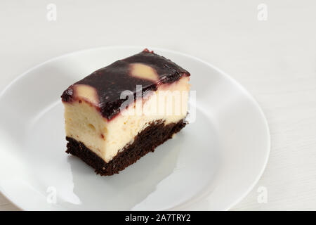 Une tranche de gâteau au fromage avec de la confiture de fruits sur le dessus. Un morceau de gâteau au chocolat avec crème et fromage doux sur plaque blanche. Banque D'Images