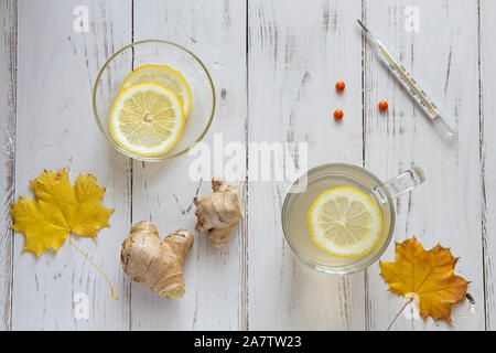 Thé au gingembre chaud avec les tranches de citron sur une assiette, feuilles d'érable de thermomètre, les pilules sont sur un tableau blanc. Banque D'Images