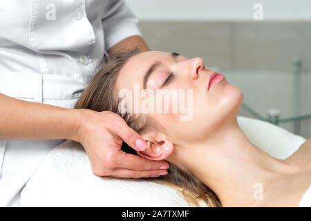 Young caucasian woman recevant un massage de la tête par des femmes de toucher les oreilles de femme esthéticienne et temples dans le spa salon de close up. Banque D'Images