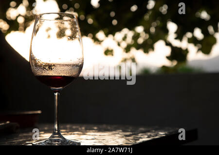 Un verre de vinaigre rouge sur la table avec le coucher du soleil dans le dos et quelques feuilles vertes Banque D'Images