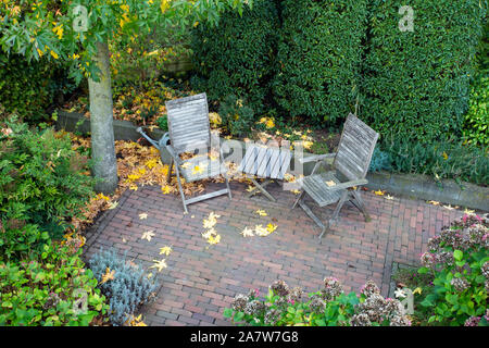 Jardin verdoyant avec table à manger en bois avec des chaises dans un coin confortable avec des feuilles tombées à l'automne Banque D'Images