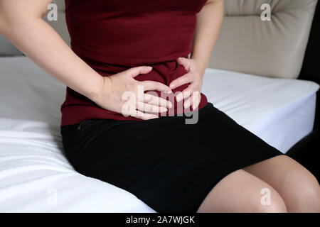 Femme souffrant de douleur dans l'abdomen. Fille Slim en jupe noire assis sur le lit, serrant son ventre concept d'indigestion, maux d'estomac, la menstruation Banque D'Images