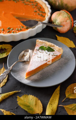 Tarte à la citrouille maison décorée avec des graines et des feuilles sèches sur fond noir. Concept de l'action de grâce ou l'automne à la lumière naturelle Banque D'Images