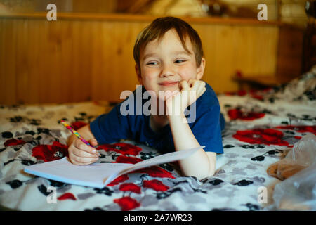 Enfant boy doing homework lying on bed Banque D'Images