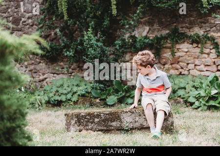 Vue avant du garçon assis sur le rocher couvert de mousse-bench Banque D'Images