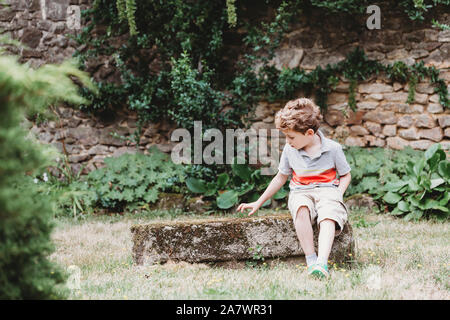 Vue avant du garçon assis sur le rocher couvert de mousse-bench Banque D'Images