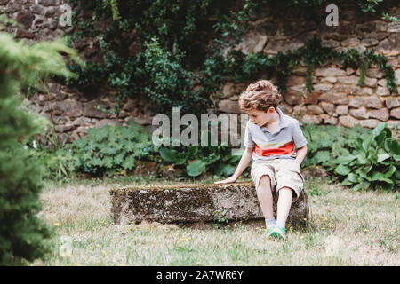 Vue avant du garçon assis sur le rocher couvert de mousse-bench Banque D'Images