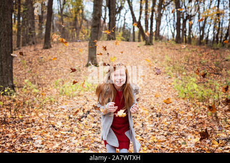 Jeune fille cheveux rouge jouer dehors dans les feuilles d'automne Banque D'Images