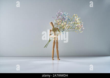 Homme de bois avec une branche de fleurs délicates sur un fond gris clair Banque D'Images