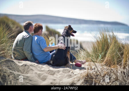 Heureux homme couple à la plage avec leur chien. Banque D'Images