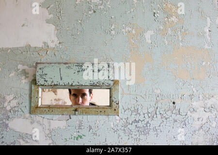 Portrait of a young woman à travers un trou dans un mur d'un bâtiment abandonné. Banque D'Images