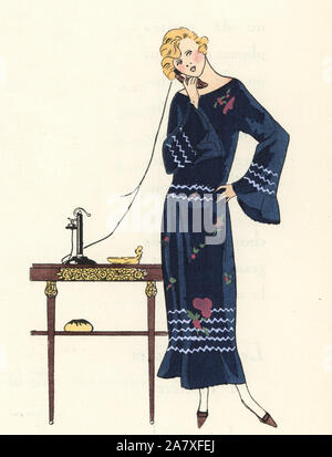 Femme au téléphone dans une robe de serge bleu brodé de fleurs. Coloriée pochoir (stencil) lithographie du magazine de mode de luxe français Art, la goutte, Beaute, 1923. Banque D'Images