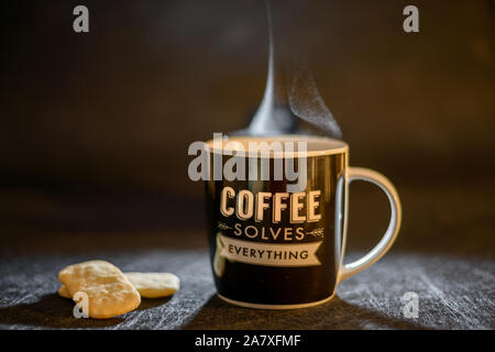 Tasse de café chaud, tasse de café résout tout sur fond sombre avec un cookie Banque D'Images