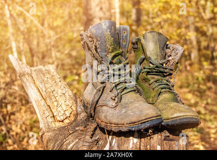 Deux fortement usé et vieux bottes militaires position contre une forêt sur une journée ensoleillée. Une paire de chaussures de travail abandonnés pourrissent sur une souche. Banque D'Images