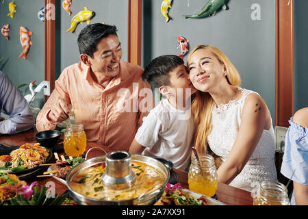 Happy cute little boy kissing vietnamien sa belle mère souriant sur la joue lorsqu'ils ont de la famille dîner au restaurant Banque D'Images