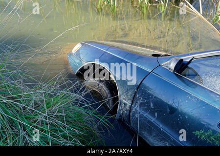 Voiture en panne et abandonné dans une zone humide, son contenu de polluer l'eau. Banque D'Images
