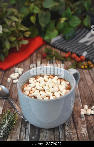 Mug gris avec boisson chocolat garnies de petits blancs les guimauves et le chocolat et la cannelle en poudre sur le bureau en bois avec décor d'hiver arrangement Banque D'Images