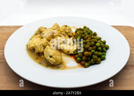 Poulet au curry servi avec des pois verts servi dans une assiette blanche, table en bois, fond blanc. Banque D'Images