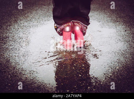Girl having fun, sauter dans l'eau flaque sur la rue mouillée, portant des bottes de pluie Avec détails réfléchants rayures tissu brillant. Une grande visibilité et sécurité i Banque D'Images