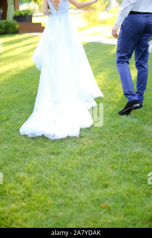 Vue arrière de la jeune mariée et se toilettent walking in park sur l'herbe verte. Banque D'Images