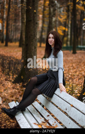 Portrait de l'automne une belle jeune femme en automne parc, assis sur le dos d'un banc blanc et profiter de l'automne, paysage gris portant des ba Banque D'Images