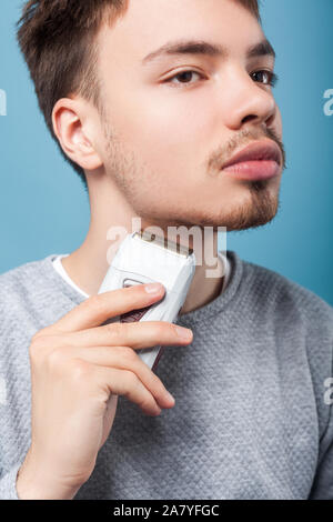 Le toilettage et les soins de la peau. Portrait de l'homme attentif porté brunette avec moustache et poils épilateur holding, l'élimination des poils du visage, de rasage pour hommes rou Banque D'Images