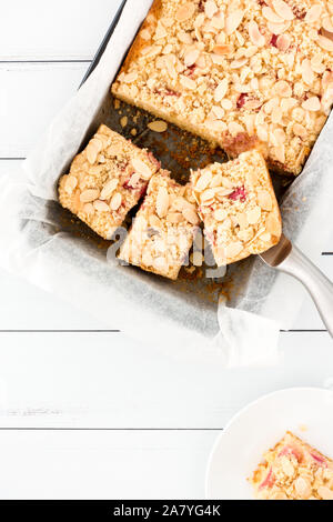 Crumble rhubarbe gâteau dans une plaque à pâtisserie recouverte de papier sulfurisé et d'un morceau sur une assiette blanche. Banque D'Images