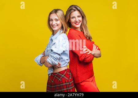 Meilleurs amis debout avec le dos à l'autre et mains croisées. Portrait de deux charmantes femmes dans des tenues élégantes smiling at camera. en Banque D'Images