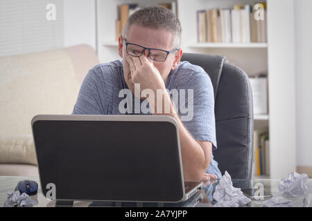 Fatigués et surmenés freelancer tenait la tête dans la main alors qu'il était assis à son lieu de travail au bureau ou à la maison Banque D'Images