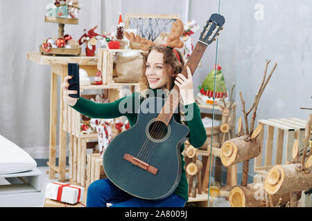 Belle jeune femme en pull-over chaud holding guitar et posant pour Noël photo Banque D'Images
