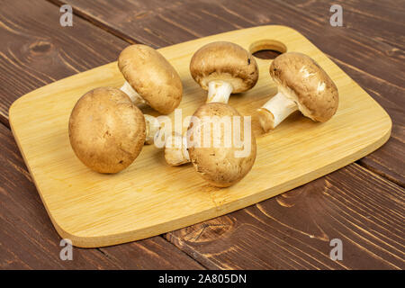 Groupe de cinq entiers et frais, champignon brun sur une planche à découper en bambou sur bois marron foncé Banque D'Images