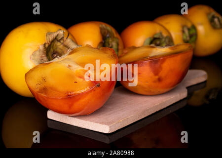 Groupe de cinq ensemble les deux moitiés d'orange sucrée persimmon sur planche à découper en bois isolé sur verre noir Banque D'Images