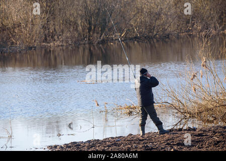 Lubana, la Lettonie. 6 avril 2019. Pêcheur de parler par téléphone, et lors de la pêche à la ligne de côte, près du lac. Banque D'Images