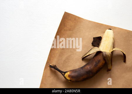 Laid de la nourriture. Vieux surmûris banana se trouve sur du papier brun sur un fond blanc. L'orientation horizontale, vue du dessus. Banque D'Images